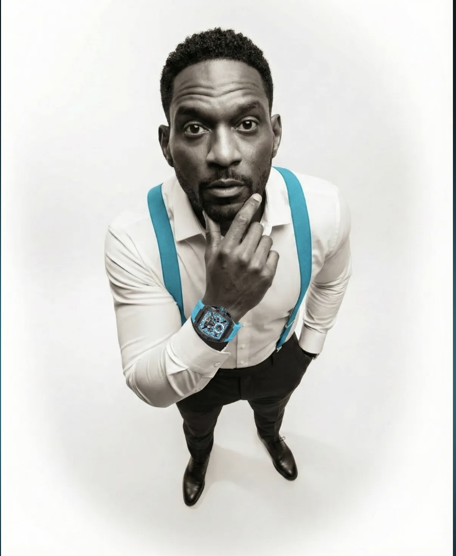 Monochrome portrait of a man in a white shirt with cyan suspenders and a cyan watch, on a soft neutral ground.